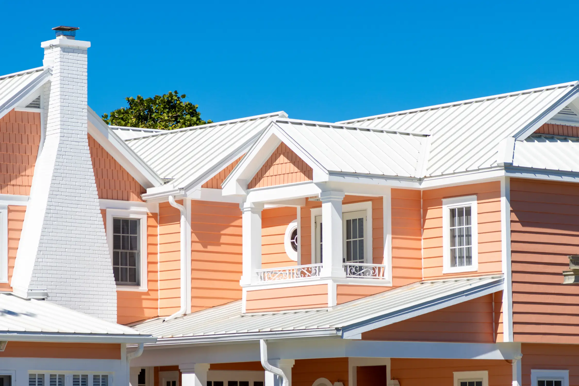 Residential home with a white standing-seam metal roof under a clear blue sky.