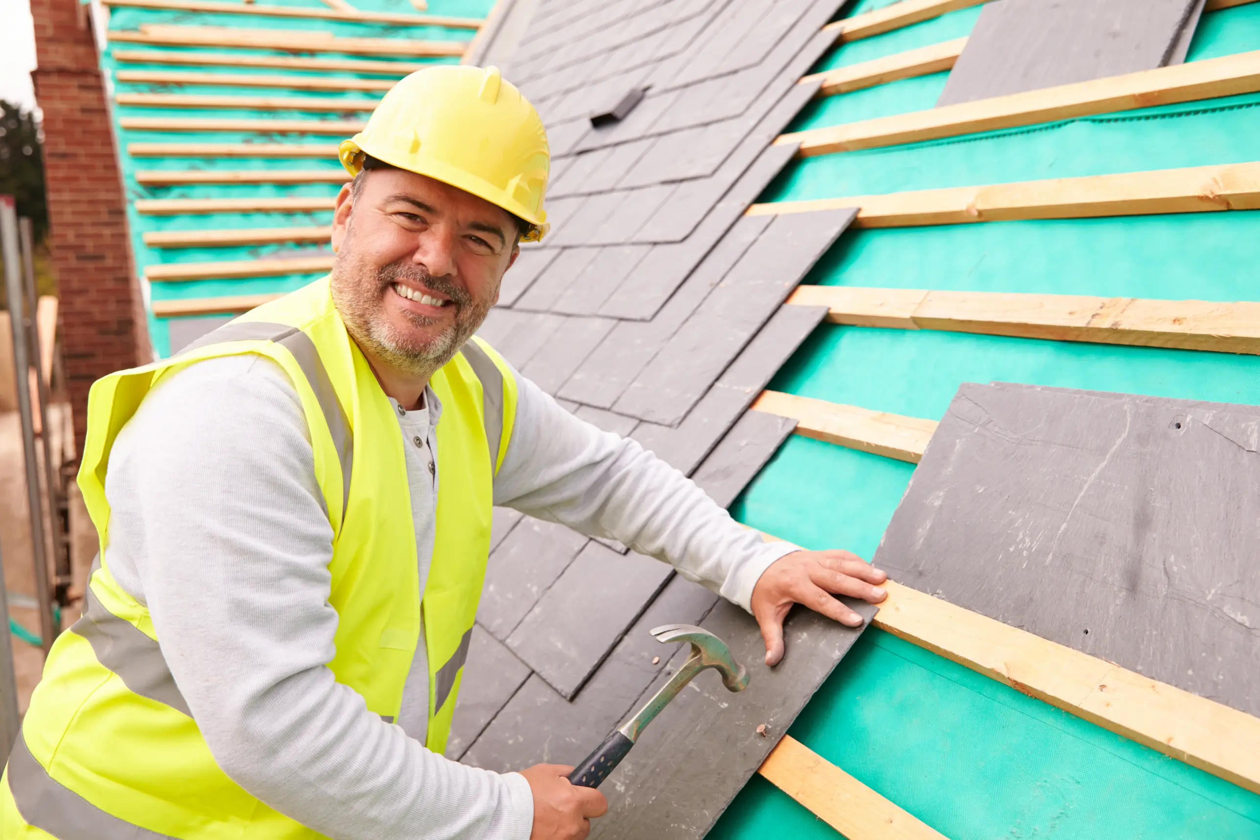 Roofer smiling while installing asphalt shingles on a residential roof.